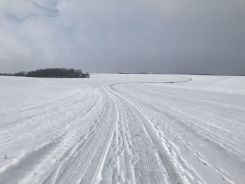 Tire tracks on snow covered field against sky