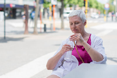 An aged woman with bob cut drink water from plastic bottle at the cafe table