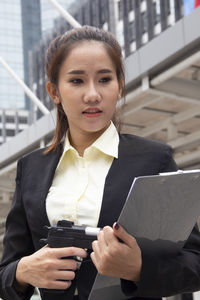 Young businesswoman holding gun and clipboard outdoors