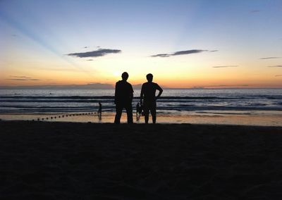 Silhouette people standing at beach against sky during sunset