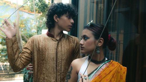 A tattooed girl and boy stand together near a window