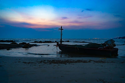 Boat moored on shore against sky during sunset