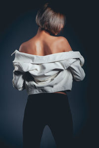 Rear view of seductive woman wearing jacket standing against black background