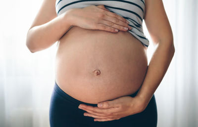 Midsection of pregnant woman standing at home