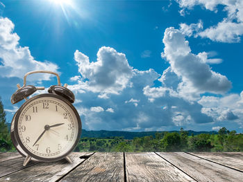 Clock on table against sky on sunny day