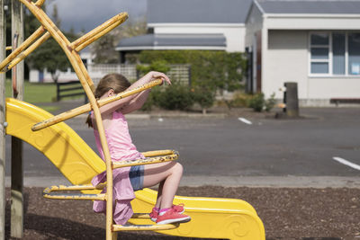 Rear view of girl sitting on yellow umbrella in city