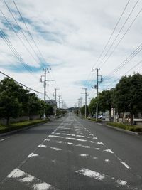 Road by electricity pylon against sky