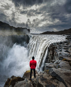 Rear view of man standing on rock by sea against sky