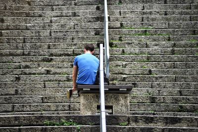 Rear view of man sitting on bench on steps