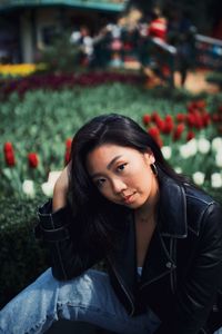 Fashionable young woman sitting against flowering plants in park