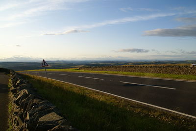 Road passing through field against sky