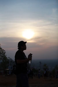 Silhouette man holding camera against sky during sunset