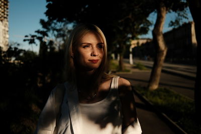 Portrait of young woman standing against trees