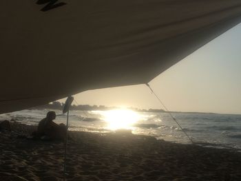 Man sitting on sea against sky during sunset