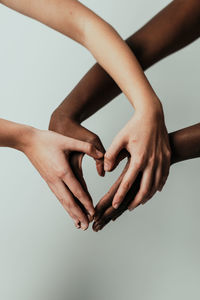 Cropped hands of women making heart shape against gray background