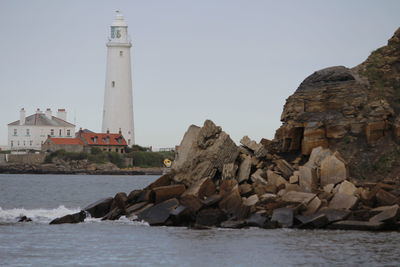Lighthouse by sea against buildings against clear sky