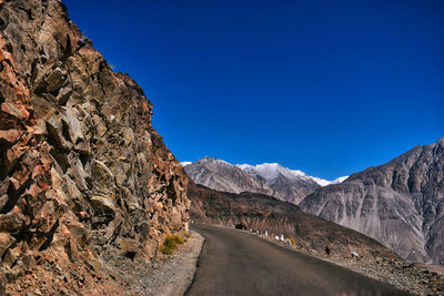 Road leading towards mountains against clear blue sky