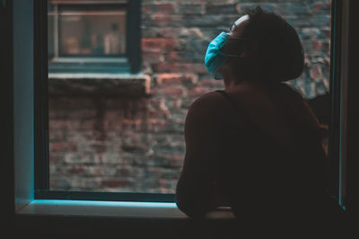 Side view of woman looking through window at home