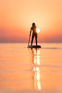 Silhouette person in sea against sky during sunset