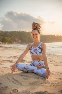 Portrait of smiling woman meditating while sitting on beach