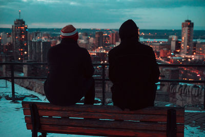 Rear view of people sitting on bench in city during winter