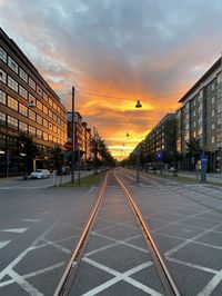 Road by buildings against sky during sunset in city