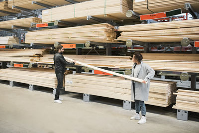 Full length of couple examining wooden plank while standing by shelves at hardware store