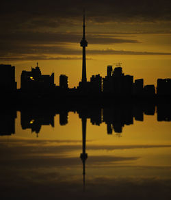 Reflection of silhouette buildings on lake against orange sky