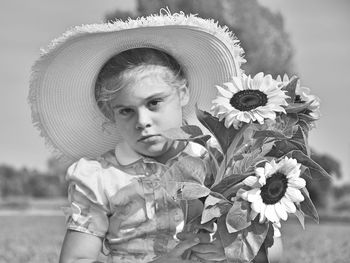 Portrait of little girl holding sunflowers on field