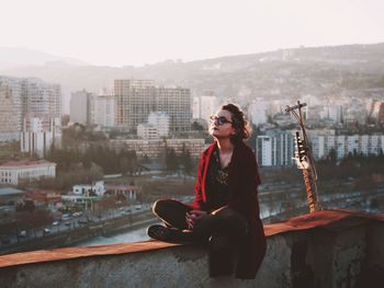 Young woman meditating while sitting on retaining wall at building terrace