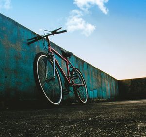 Bicycle parked by wall on field against sky