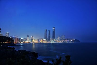 Illuminated city by sea against sky at night