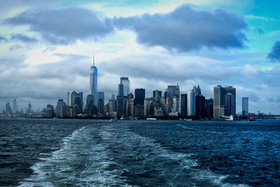 Sea and buildings in city against cloudy sky