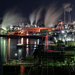 Illuminated factory by river against sky at night