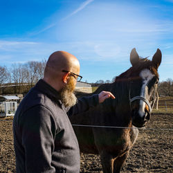 Man standing with horse standing at ranch against sky