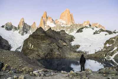 Rear view of person standing on rock against snowcapped mountain range