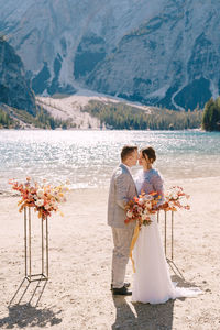 Rear view of friends standing at shore against mountains