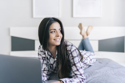 Portrait of smiling woman sitting on bed at home