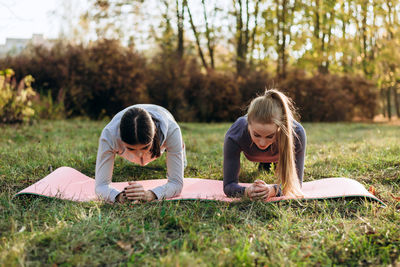 Two girlfriends are doing fitness plank in the park.