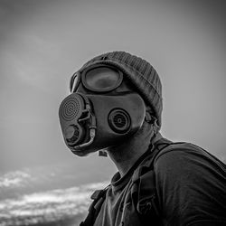 Young man wearing gas mask against sky