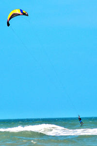 Person paragliding over sea against clear sky