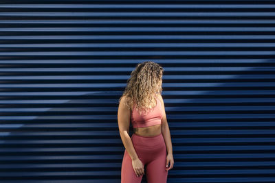 Young sportswoman with curly hair standing in front of blue wall