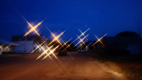 Illuminated road against clear blue sky at night