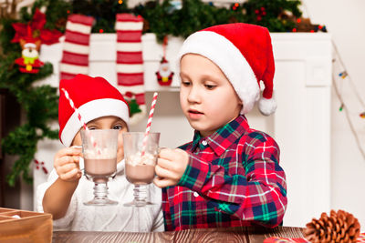 Cute sibling wearing santa hat toasting milkshake at home 