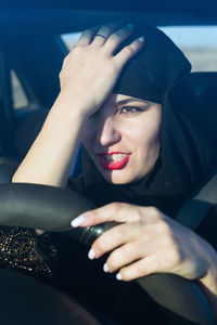 Close-up of woman wearing hijab with head in hand driving car seen through windshield