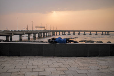 Rear view of man sitting on street by sea against sky