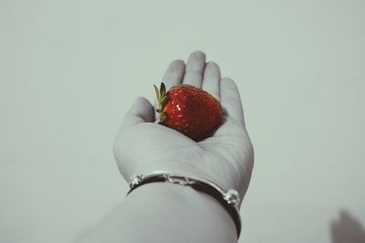 Cropped image of woman with strawberry on palm against white background