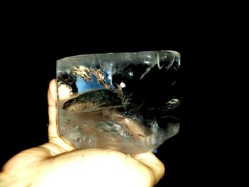 Close-up of human hand holding object over black background