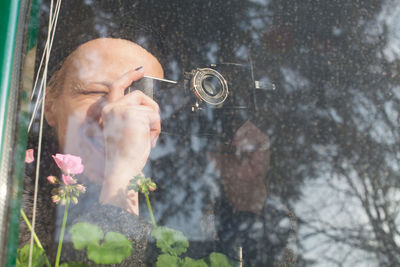 Mature woman photographing with vintage camera seen through window