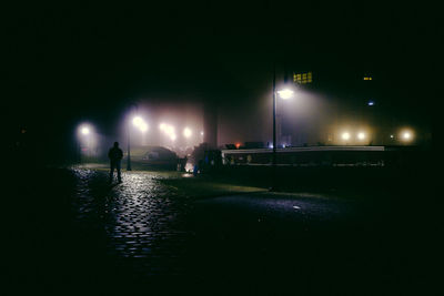 Silhouette man on illuminated street against sky at night